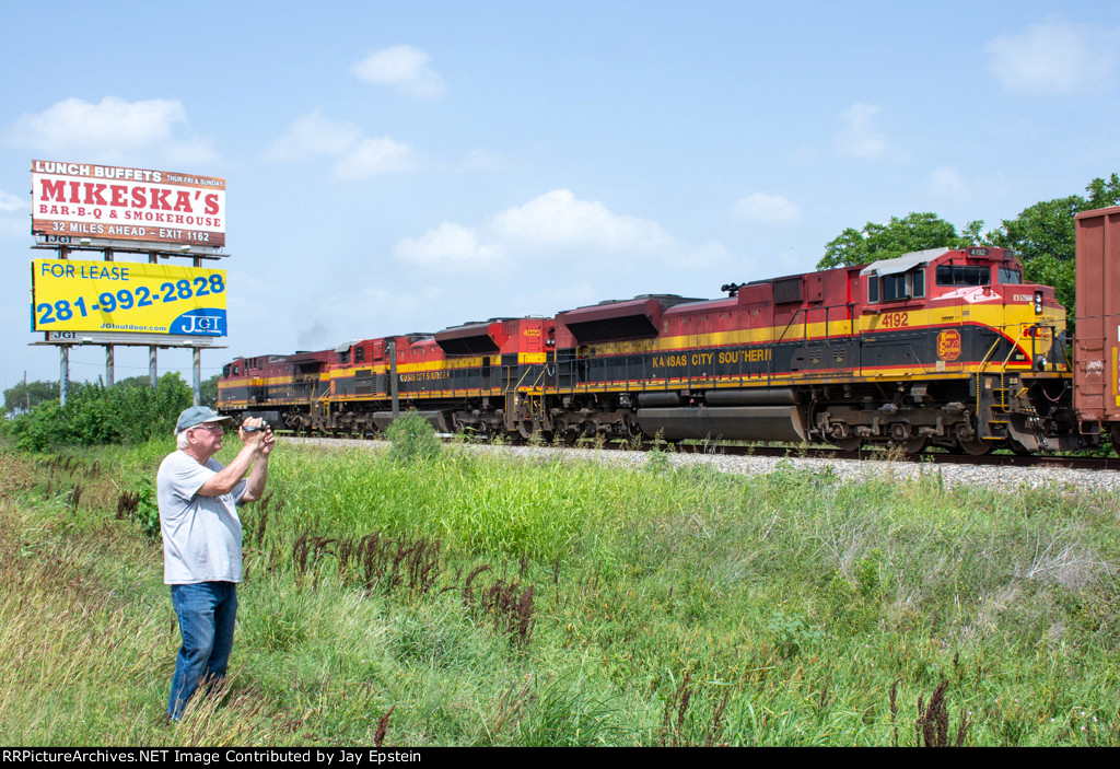 Three KCS engines rumble past a railfan and some billboards 